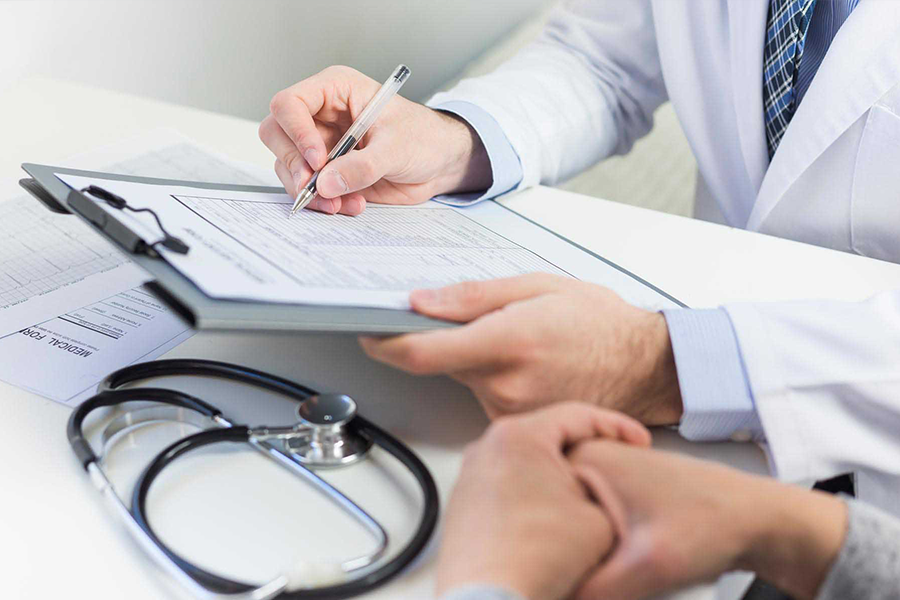 A doctor in a white coat is writing on a clipboard inside an office, surrounded by medical equipment and office supplies.
